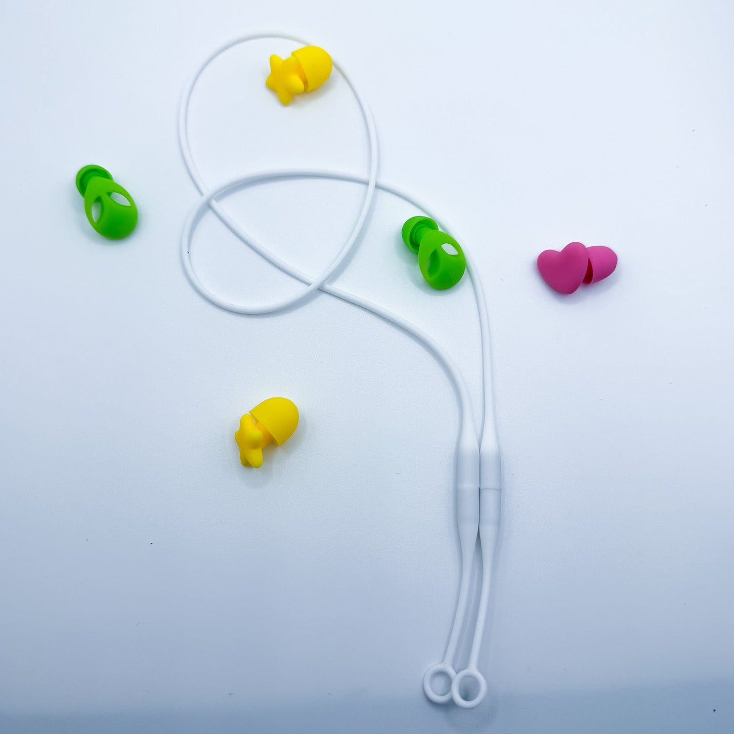 White silicone earplug cord with green, yellow, and pink silicone tips arranged on a light blue-white background.