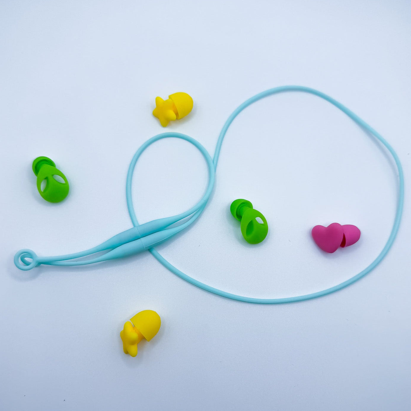 A pair of light blue silicone earplug connector cord with small colorful ear tips in green, yellow, and pink, arranged on a light gray background.