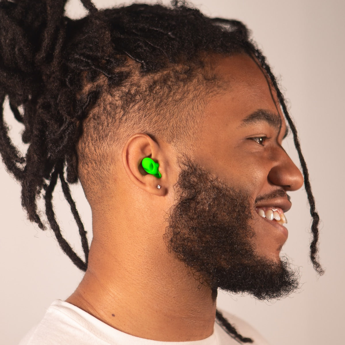 Green alien-shaped Charm'd earplugs, a reusable pair shown against a soft studio backdrop